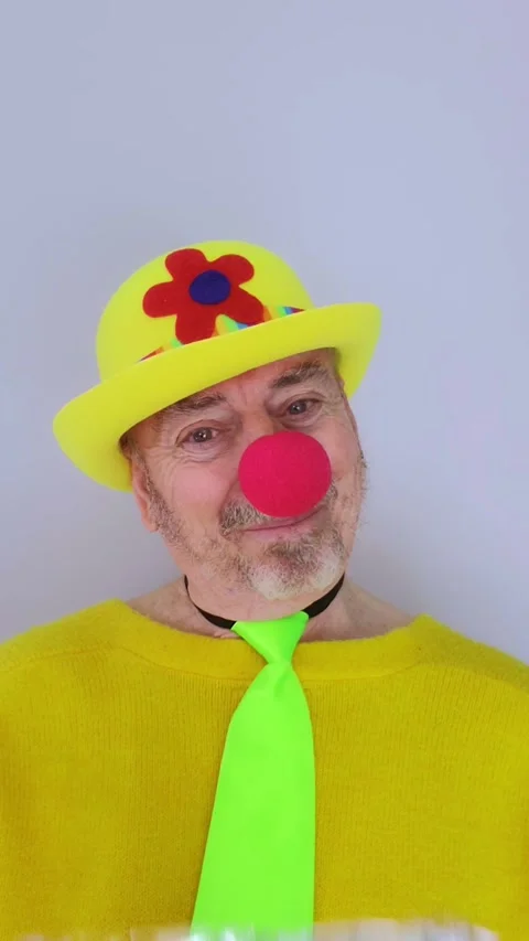 Elderly man dressed as a clown throws an exploding bag of confetti at the camera 動画素材 330802739