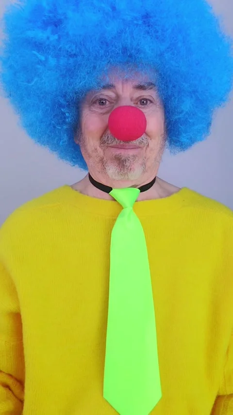 Elderly man dressed as a funny clown is making silly faces on a white background Stock Footage 330802763