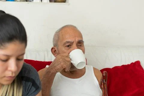 Elderly man drinking coffee while young woman sits beside him sharing relax.. Stockfoto's