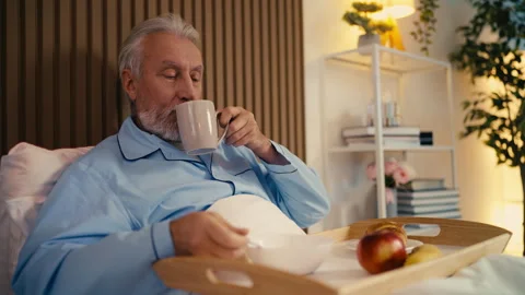 Elderly man eating breakfast and drinking tea while lying in hospital bed Stock Footage 279177718