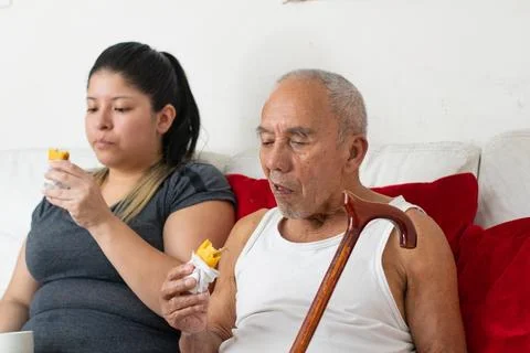 Elderly man eating empanada while sitting beside young woman sharing everyd.. Фото