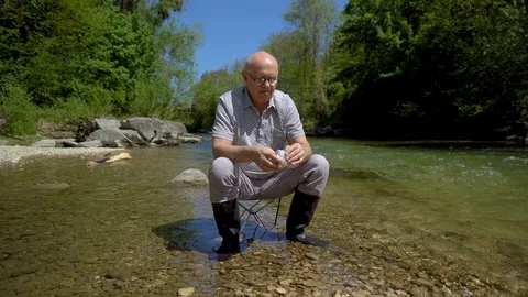 Elderly Man Eating Sandwich While Sitting on Chair in River in Beautiful Nature Stock Footage 112637997