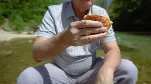 Elderly Man Eating Sandwich While Sitting on Chair in River in Beautiful Nature Stock Footage 112695719