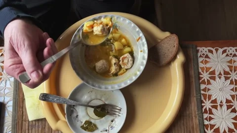 An elderly man eats soup with meatballs and bread at a table on a tray. Top view Stock Footage 233570504