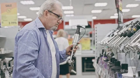 An elderly man in an electronics hypermarket chooses a blender. A pensioner Stock Footage 252080321
