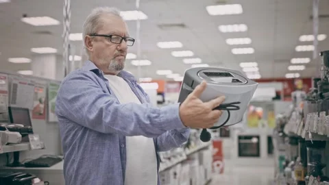 An elderly man in an electronics hypermarket holding a toaster. A pensioner Stock Footage 250443310