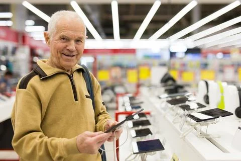Elderly man examines tablet computer in showroom of electronics store Stock Photos