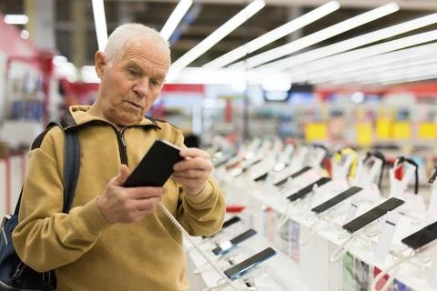 Elderly man examines tablet computer in showroom of electronics store Stock Photos