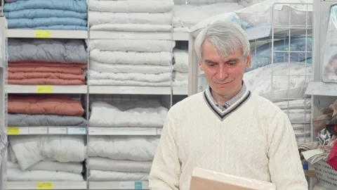Elderly man exploring vibrant bedroom textiles at a cozy furnishings store Stock Footage 311201083