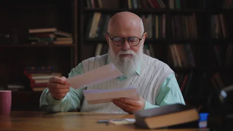 Elderly man in eyeglasses sorting mail in his study, checking monthly bills Stock Footage 320671232