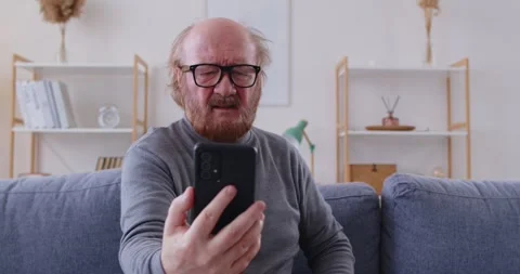 Elderly man with eyesight problems and in eyeglasses looking at his mobile phone Stock Footage 309283465