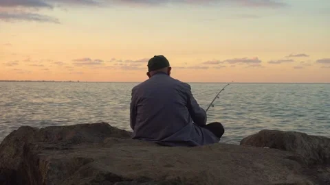 Elderly Man Fishing with Rod on Rocks by the Sea at Sunset Stock Footage 302677053