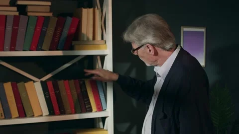 An elderly man in glasses is selecting a book to read. An old man is standing Video stock 132635901