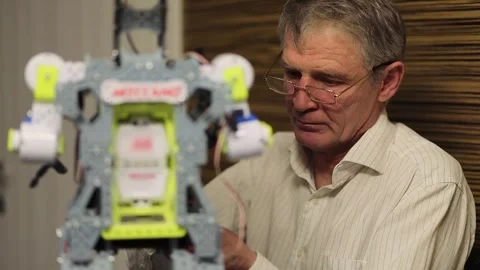 Elderly man in glasses setups small robot. Slow motion Stock Footage 276369284