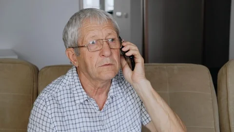 An elderly man in glasses is sitting on the sofa and talking on the phone. Stock Footage 111060955