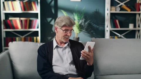 An elderly man in glasses is talking over the tablet and nodding his head to Видео 132634979