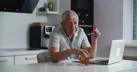 An elderly man in glasses is talking while sitting in the kitchen, next to a Stock Footage 147555210