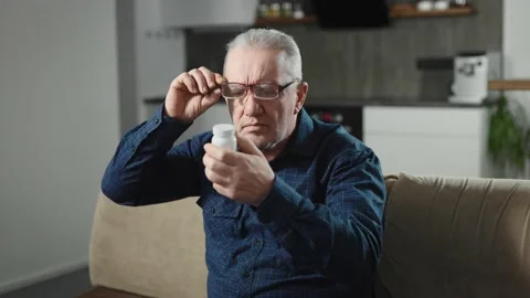 An elderly man with glasses trying to read the fine print on a drug package. A Stock Footage 236468477