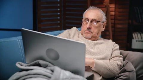 Elderly man with glasses for vision correction working with laptop at home in Stock Footage 279770255