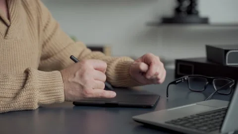 An elderly man with a gray beard draws with a pen on a tablet at home in the Stock Footage 142751612