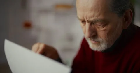 Elderly man with gray beard reading a document indoors in soft natural light Stock Footage 336276382