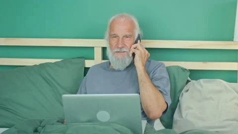 An Elderly Man Has Fun Talking on the Phone, Works Remotely Using a Laptop Video stock 164413356