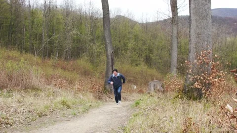 An elderly man in a hat and with a backpack on his shoulders runs along a mounta Stock Footage 237634626