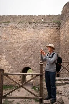 Elderly man in hat visiting medieval fortress taking photo for memory using m Stock Photos