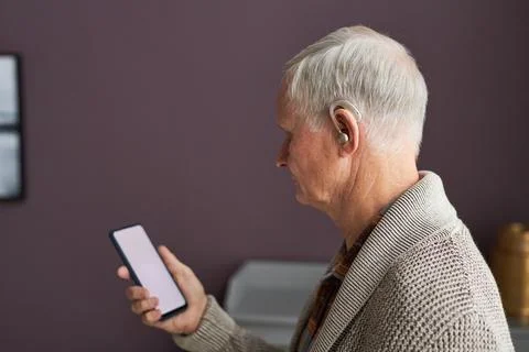 Elderly man with hearing aid listening audio on smartphone Stock Photos
