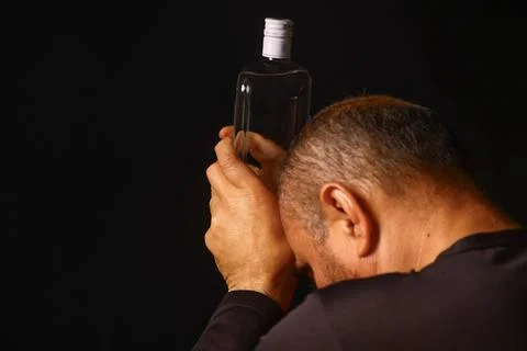 Elderly man holding a bottle in a moment of emotional exhaustion Stock Photos