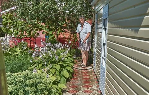 An elderly man is hosing down the sidewalk at the dacha Stock Photos