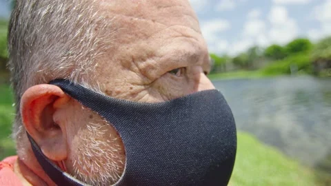 Elderly man with intense look wearing a protective face mask in front of a lake Stock Footage 131060465