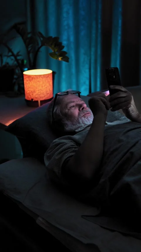 Elderly man laying in bed and very emotion react to video content on his phone Video stock 329276559