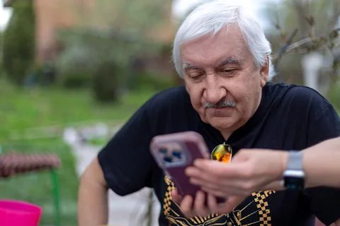 Elderly Man Learning to Use Smartphone Outdoors. Senior man being shown how to Foto stock