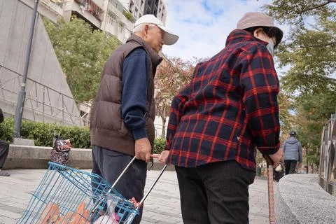 Elderly Man Looking Down at Grocery Cart Beside Wife Taipei Winter Street Stock-Fotos