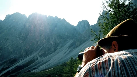 Elderly man looks through the binoculars towards the mountains Stockbeeldmateriaal 94620638