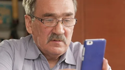 An elderly man with a mustache in glasses dials a text message on his mobile Stock Footage 74932326