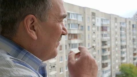 Elderly man with a mustache smoking on the balcony. One can see the multi-storey Stock Footage 70133341