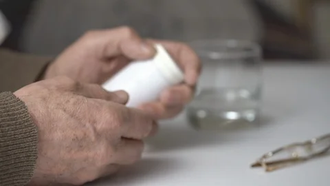 Elderly man opens plastic bottle with pills at white table Stock-Footage 125016687