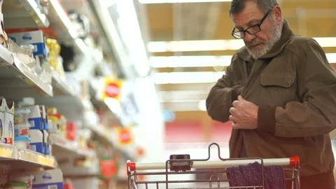 Elderly man pensioner with a gray beard and glasses picks out a cheese in a Stock Footage 101355392