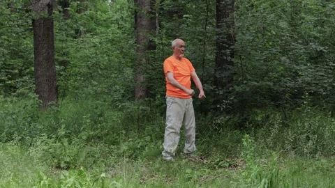 An elderly man performs circular punches against a natural backdrop Stock Footage 310931347