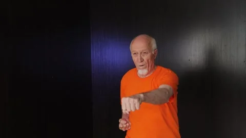An elderly man performs punches with a change of stance while jumping Stock Footage 312096793