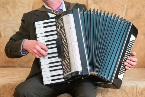 Elderly Man Playing Accordion While Sitting on a Couch in Cozy Living Room. Stock Photos