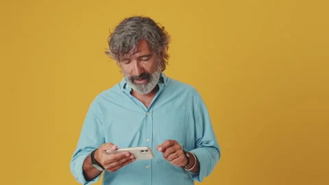 Elderly man playing and winning a video game on a mobile phone, isolated on an Stock Footage 252503441