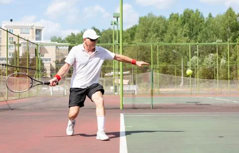 An elderly man plays tennis on an outdoor court Stock Photos