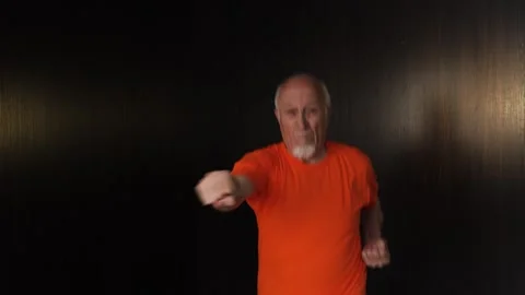 An elderly man practices punches with a change of stance while jumping Stock Footage 312096789