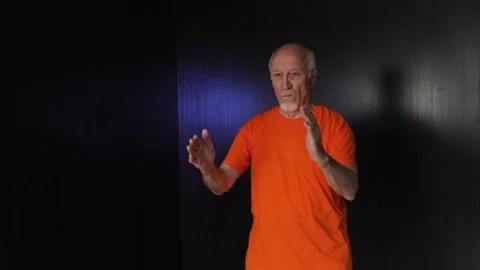 An elderly man practices side kicks with his knees to his palms Stock Footage 312096792