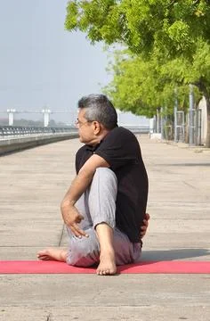 Elderly man practicing Ardha Matsyendrasana - Half Lord of the Fishes Pose Stock Photos
