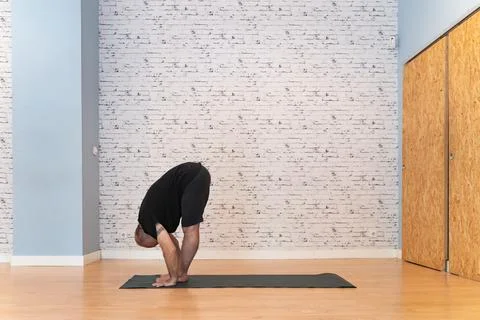 Elderly man practicing a deep forward bend yoga pose on a mat in a bright room. Fotos Stock