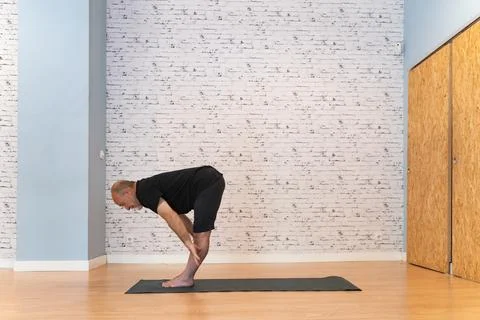 Elderly man practicing a forward bend yoga pose on a mat in a bright, spacious 스톡 사진